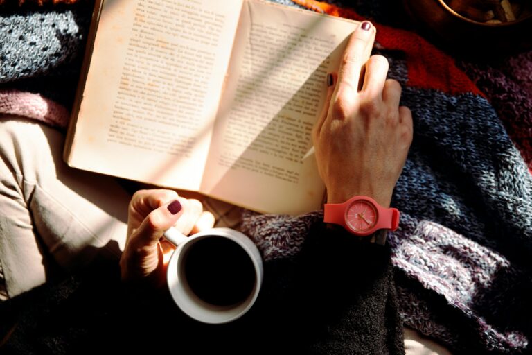 Woman relaxing with a book and coffee in a sunlit cozy setting, wearing a stylish watch.